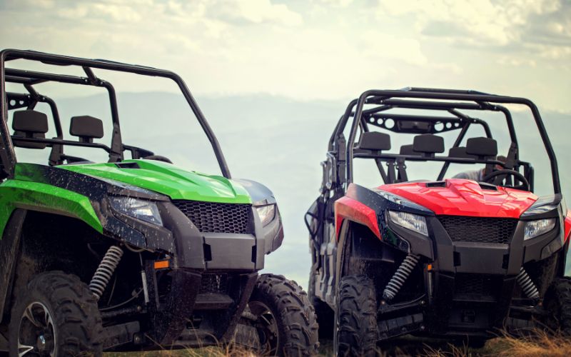 2 atvs side by side, one is red one is green